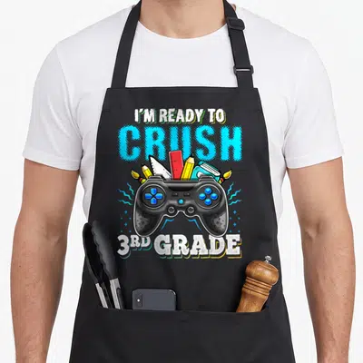 Crush 3rd video game apron - Controller holding pencils ruler notebook and brushes with I'm Ready to Crush 3rd Grade — shown on a black cotton canvas apron against a white background