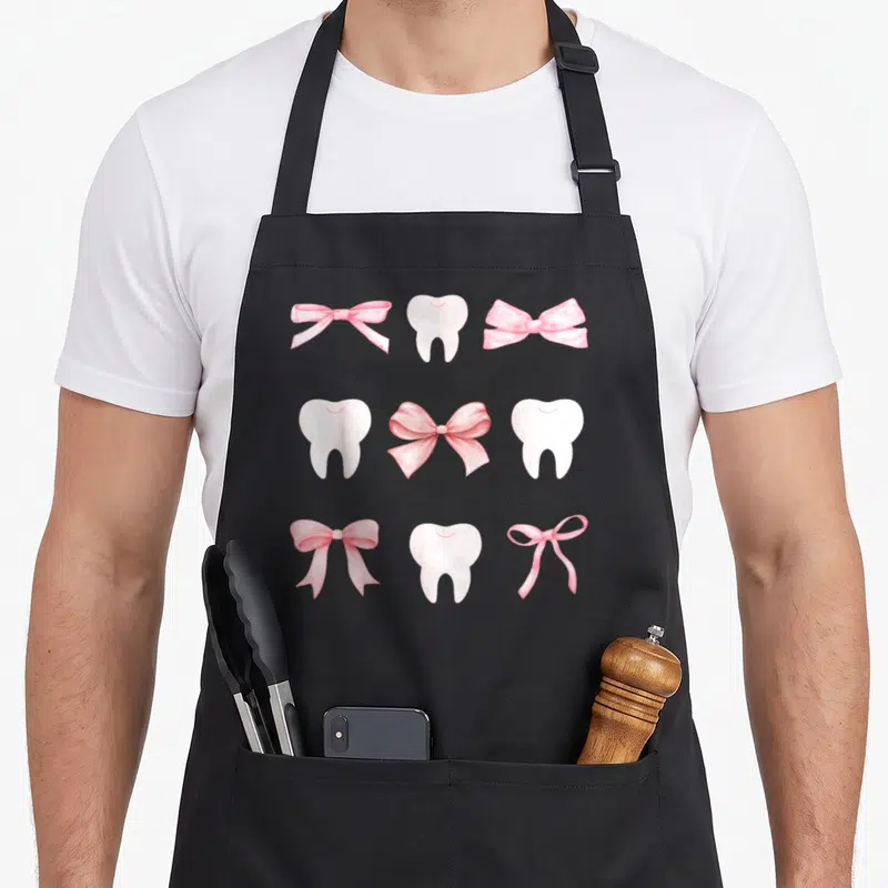 Tooth hygienist mom apron - Nine pink bows and white teeth arranged in an alternating 3x3 grid pattern — shown on a black cotton canvas apron against a white background