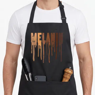 Melanin pride apron - MELANIN text in light and dark brown with vertical drip effects — shown on a black cotton canvas apron against a white background