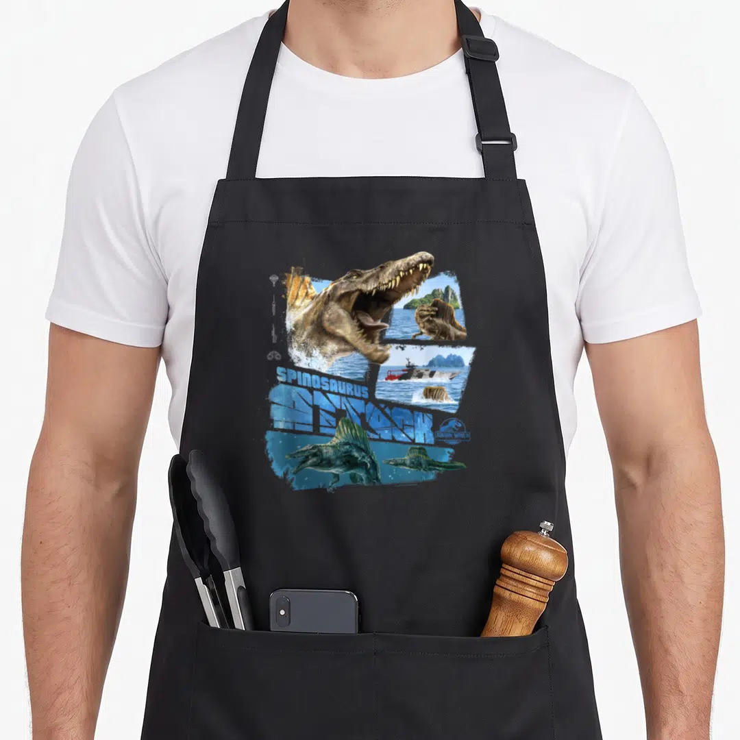 Attack spinosaurus apron - Spinosaurus head and boat collage with blue SPINOSAURUS RESEARCH text — shown on a black cotton canvas apron against a white background