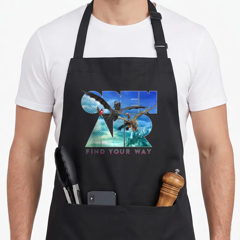Train open apron - OPEN AIR text filled with landscape, two dragons flying through letters, FIND YOUR WAY in pink — shown on a black cotton canvas apron against a white background
