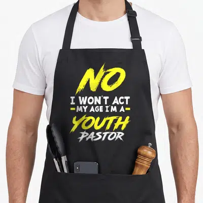 Wont christian apron - Yellow and white stacked text reading No I Won't Act My Age I'm A Youth Pastor — shown on a black cotton canvas apron against a white background