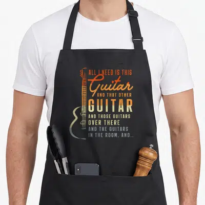 Guitar music dad apron - Distressed orange and beige text next to a blue-grey guitar neck on a dark background — shown on a black cotton canvas apron against a white background