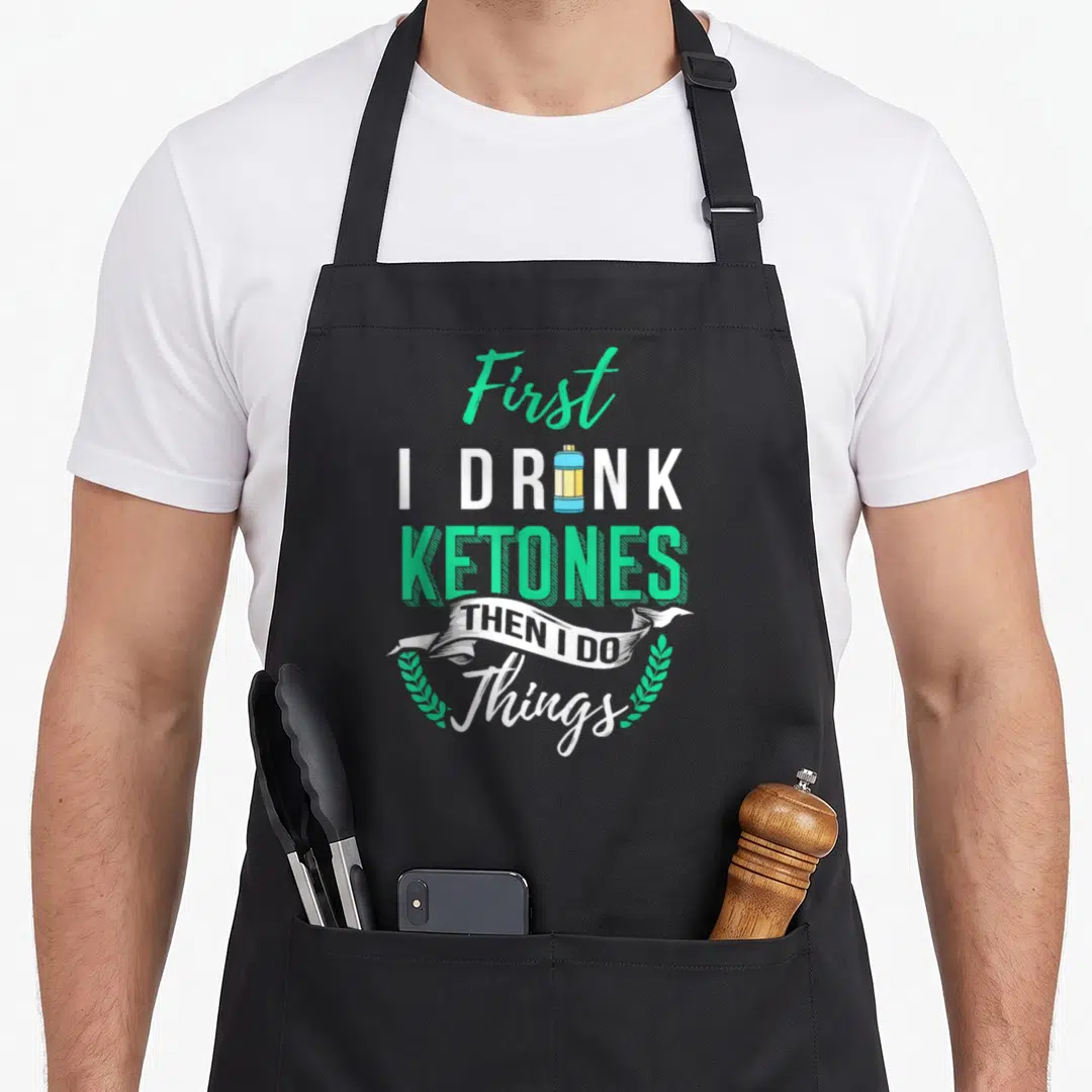 Drink lifestyle apron - Stacked text First I Drink Ketones Then I Do with water bottle icon and laurel wreath — shown on a black cotton canvas apron against a white background