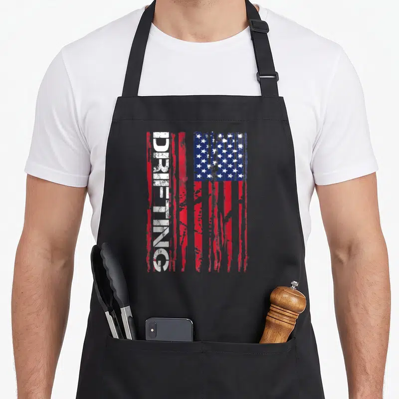 Drifting american flag apron - Vertical distressed USA flag with white DRIFTING text overlapping red stripes — shown on a black cotton canvas apron against a white background