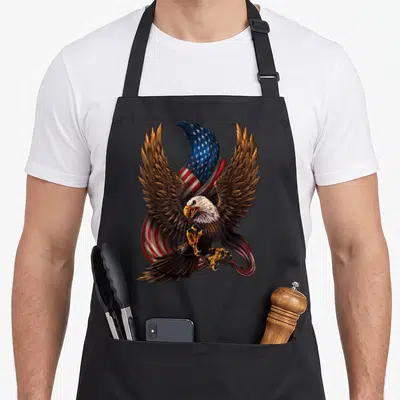 Eagle patriotic aprons - Realistic bald eagle with bare talons in front of a waving American flag in brown and flag — shown on a black cotton canvas apron against a white background