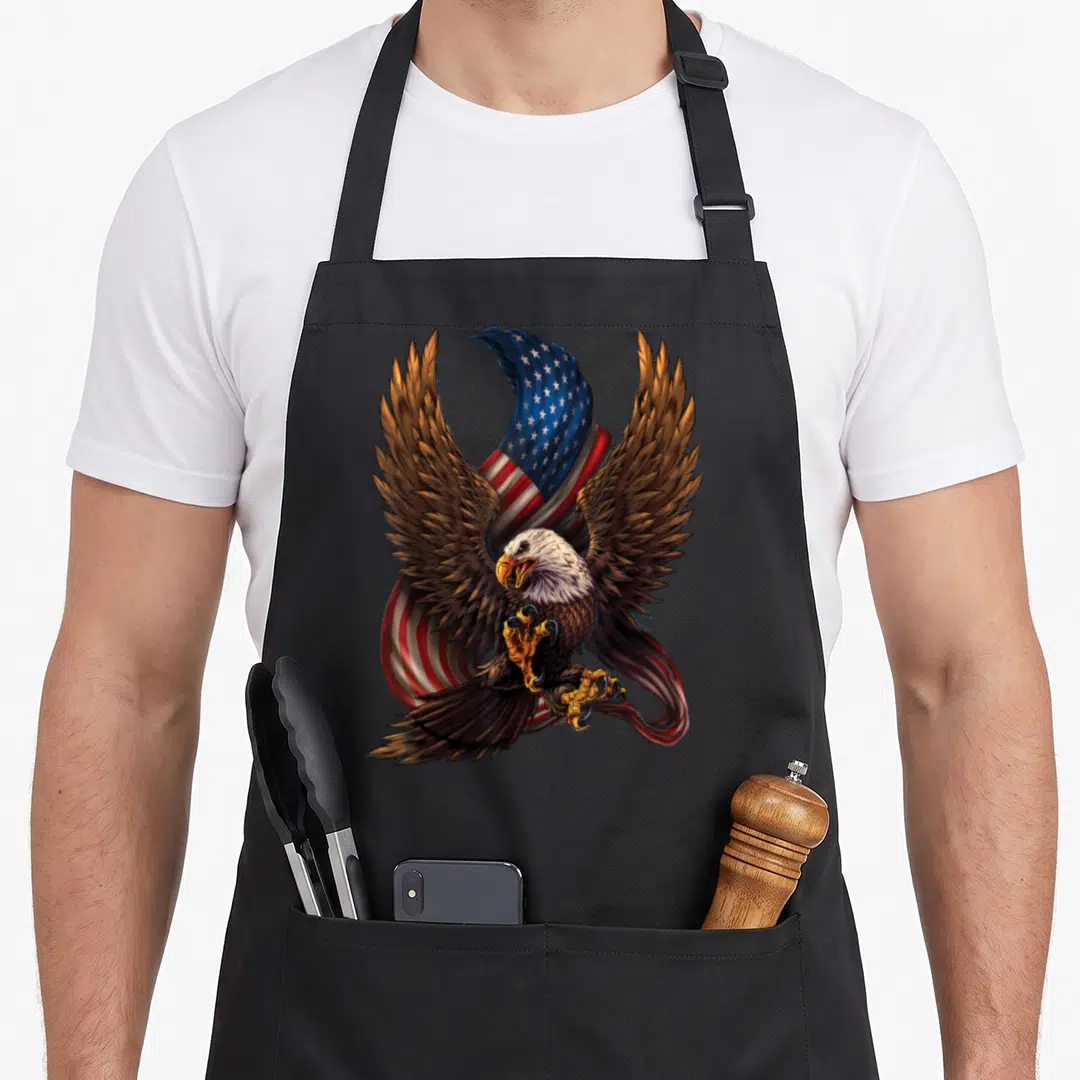Eagle patriotic aprons - Realistic bald eagle with bare talons in front of a waving American flag in brown and flag — shown on a black cotton canvas apron against a white background