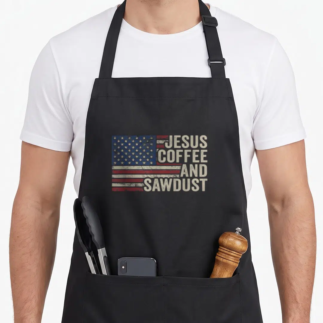 Jesus woodworking apron - Distressed USA flag beside stacked beige text JESUS COFFEE AND SAWDUST — shown on a black cotton canvas apron against a white background