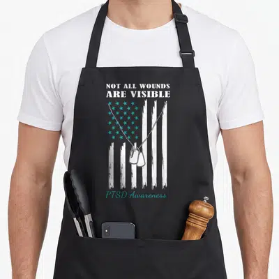 Flag ptsd awareness apron - Distressed USA flag with teal stars, two dog tags, and PTSD Awareness text — shown on a black cotton canvas apron against a white background