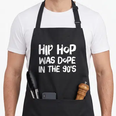 Dope hip apron - White stacked text reading HIP HOP WAS DOPE IN THE 90'S on black fabric — shown on a black cotton canvas apron against a white background