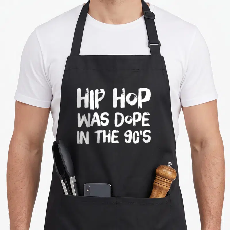 Dope hip apron - White stacked text reading HIP HOP WAS DOPE IN THE 90'S on black fabric — shown on a black cotton canvas apron against a white background