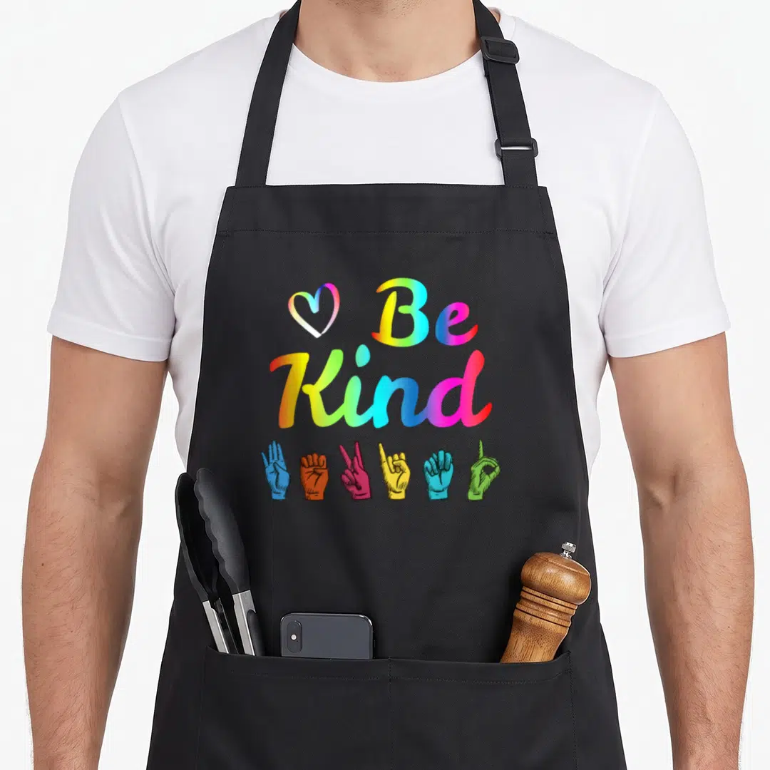 Nonverbal asl sign for apron - Rainbow 'Be Kind' text with heart and six colored ASL hand signs at bottom — shown on a black cotton canvas apron against a white background