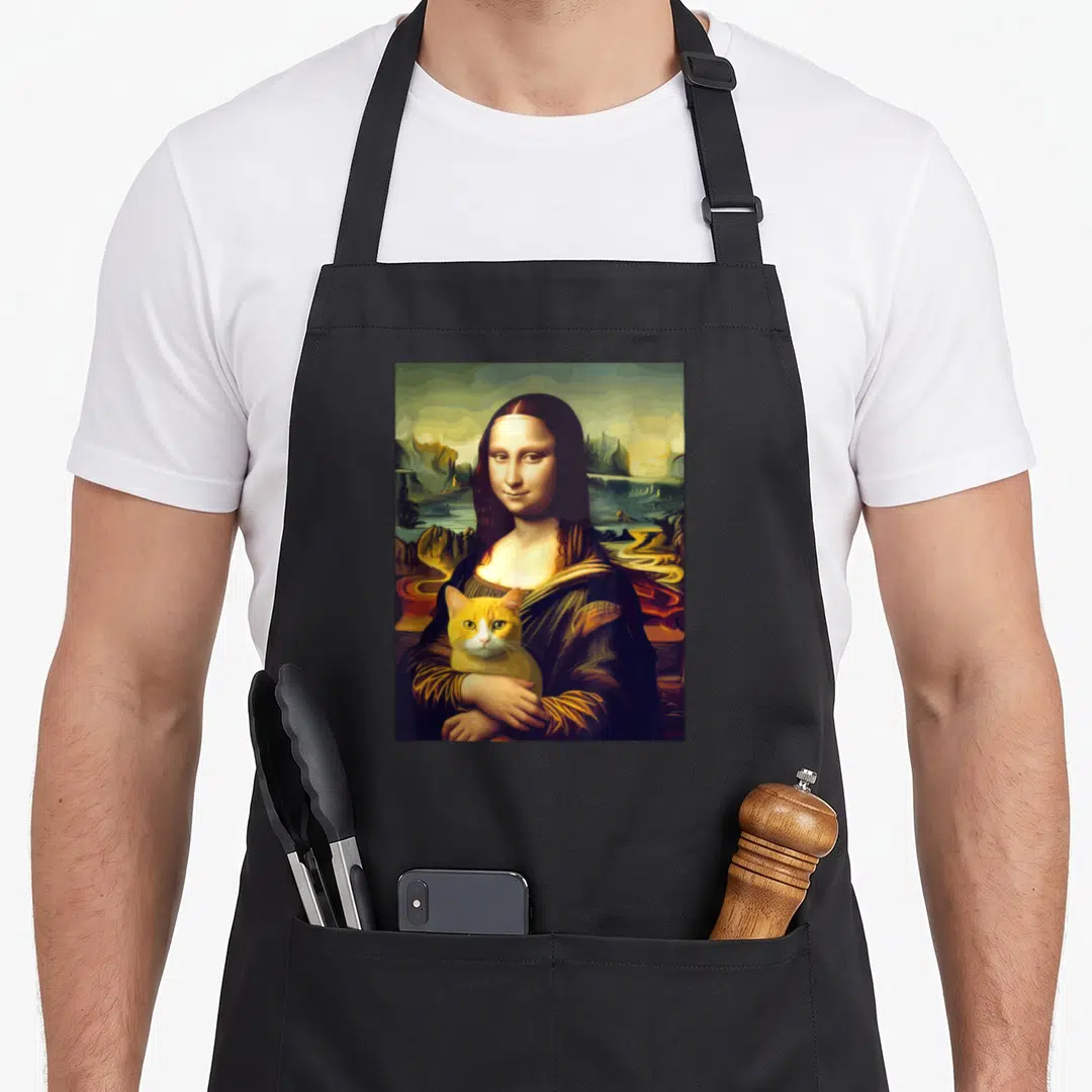 Leonardo cat holding apron - Mona Lisa figure holding orange and white cat against green landscape — shown on a black cotton canvas apron against a white background