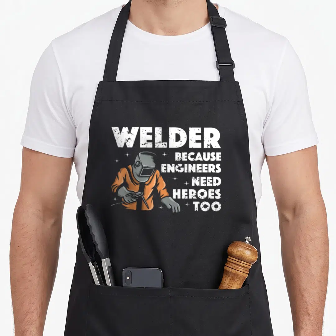 Welding mig metal worker apron - Distressed WELDER text and orange-clad welder figure holding torch beside stacked — shown on a black cotton canvas apron against a white background