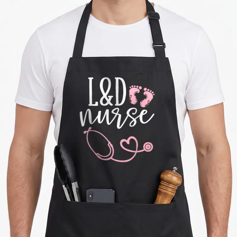 Labor nurse apron - L&D nurse text with pink footprints and stethoscope heart graphic — shown on a black cotton canvas apron against a white background