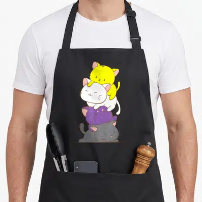 Kawaii kitten apron - Four cartoon cats stacked vertically in yellow, white, purple, grey representing non-binary pride — shown on a black cotton canvas apron against a white background