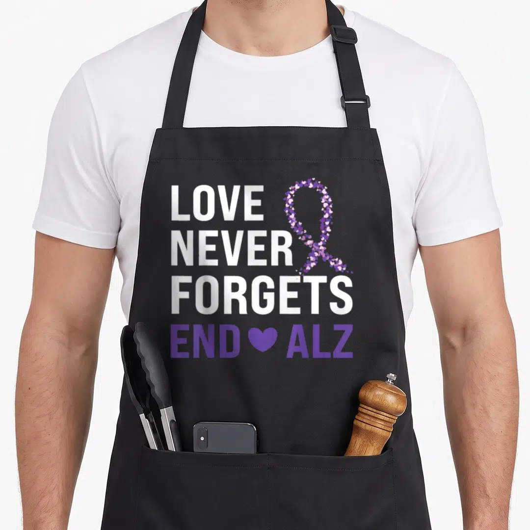 Ribbon grandpa apron - LOVE NEVER FORGETS END ALZ text with purple heart ribbon and single heart symbol — shown on a black cotton canvas apron against a white background