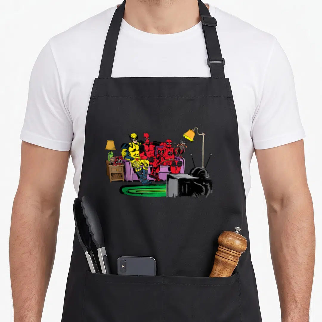 Couch gag aprons - Cartoon Deadpool and Wolverine sitting on purple couch with TV and lamp in living room scene — shown on a black cotton canvas apron against a white background