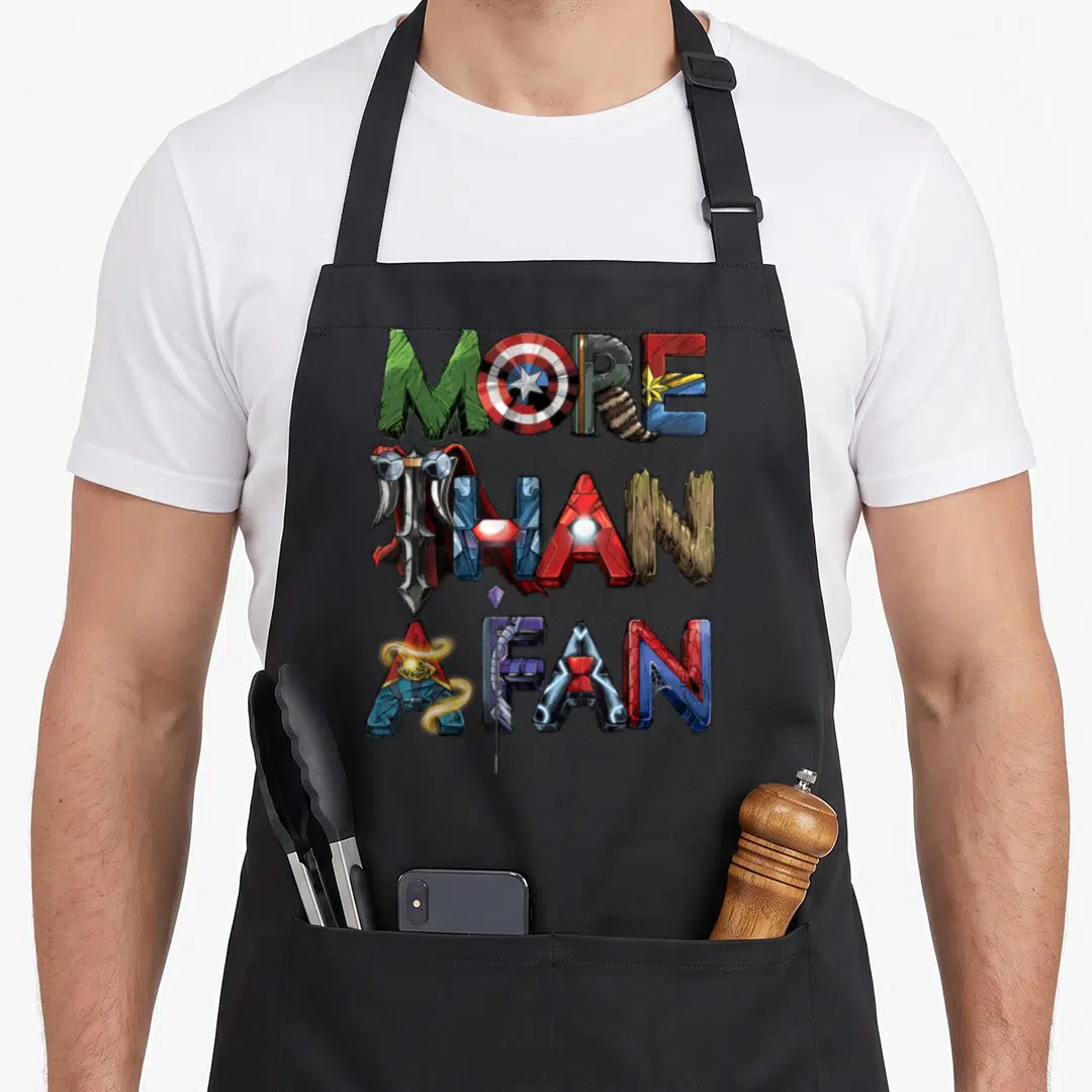 Fan novelty apron - Stacked 3D text letters styled as superheroes in red, blue, green, gold, and purple — shown on a black cotton canvas apron against a white background