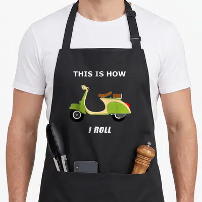 Moped italian apron - Green scooter illustration with This Is How I Roll text above and below — shown on a black cotton canvas apron against a white background