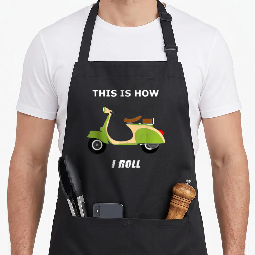 Moped italian apron - Green scooter illustration with This Is How I Roll text above and below — shown on a black cotton canvas apron against a white background