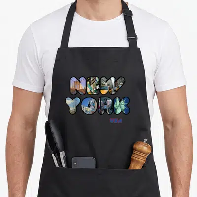 Statue liberty new york apron - NEW YORK letters filled with city photos and red USA text below — shown on a black cotton canvas apron against a white background
