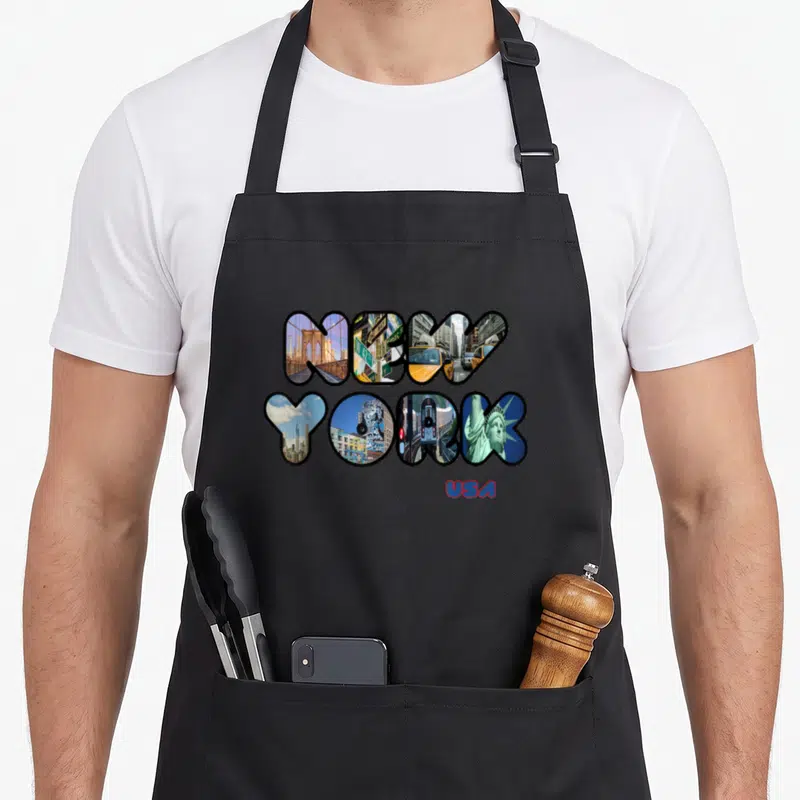 Statue liberty new york apron - NEW YORK letters filled with city photos and red USA text below — shown on a black cotton canvas apron against a white background