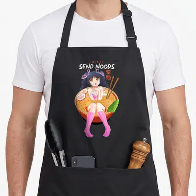 Noodle pasta apron - Anime girl in ramen bowl with SEND NOODS text and red kanji — shown on a black cotton canvas apron against a white background