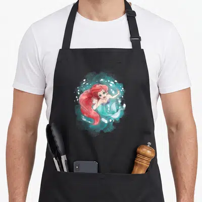 Cute ariel mermaid apron - Mermaid with red hair in teal watercolor splash with white bubbles — shown on a black cotton canvas apron against a white background