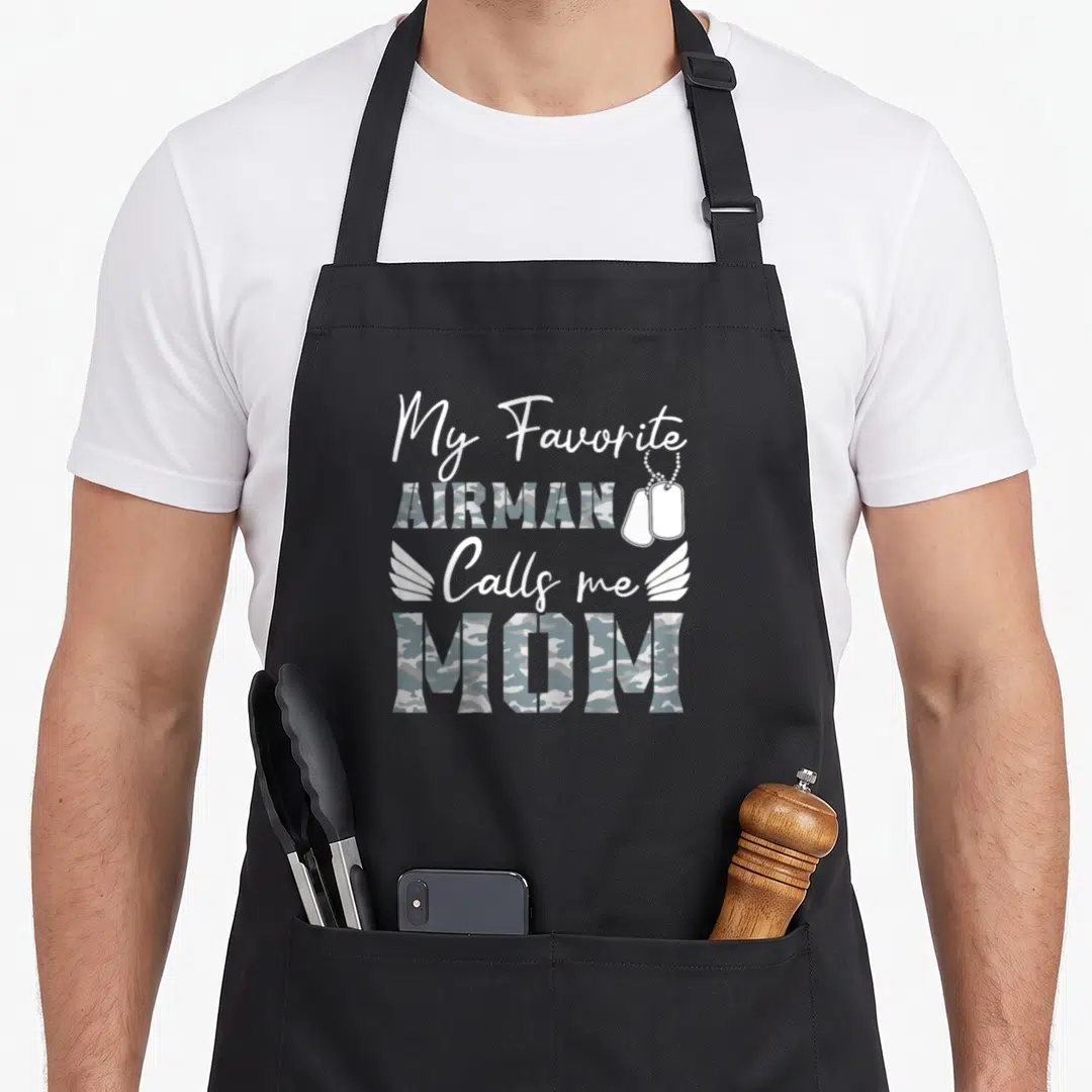 Airman mother's apron - Text My Favorite AIRMAN Calls me MOM with camo fill, dog tags, and wings on grey — shown on a black cotton canvas apron against a white background