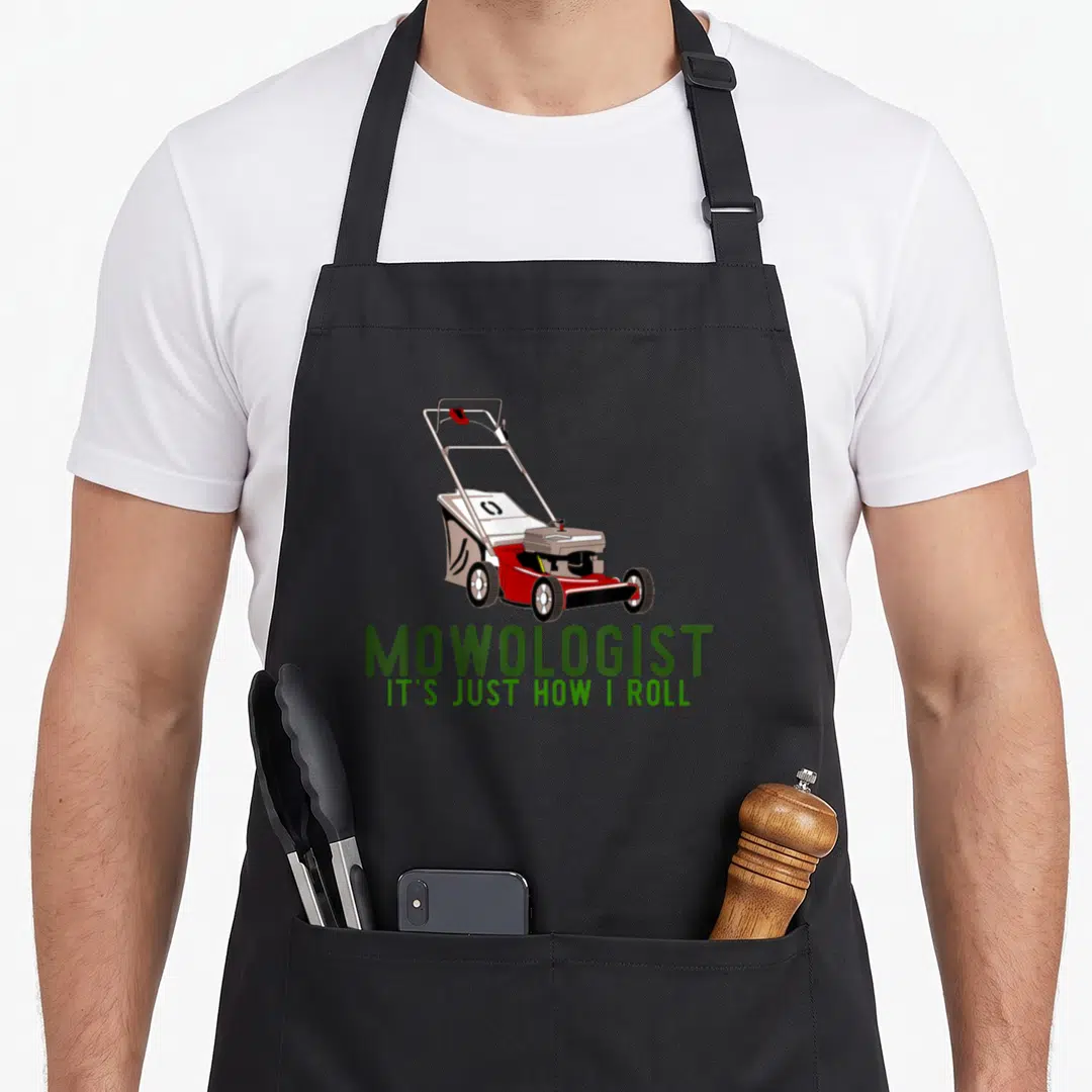 Mowologist lawn apron - Cartoon red and white lawn mower above green MOWOLOGIST text — shown on a black cotton canvas apron against a white background
