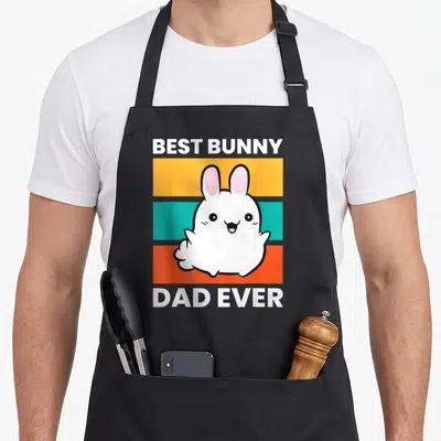 Papa bunny apron - Cartoon white rabbit on yellow teal orange stripes with text BEST BUNNY DAD EVER — shown on a black cotton canvas apron against a white background