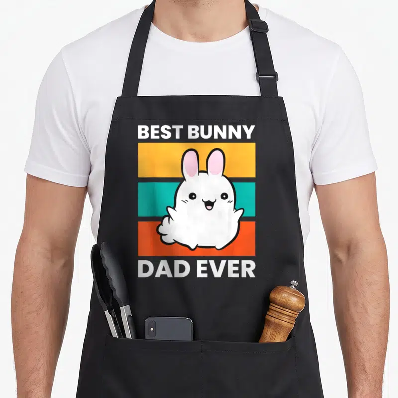 Papa bunny apron - Cartoon white rabbit on yellow teal orange stripes with text BEST BUNNY DAD EVER — shown on a black cotton canvas apron against a white background