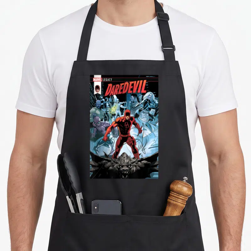 Daredevil book apron - Daredevil title text above red hero standing on stone gargoyle with city skyline background — shown on a black cotton canvas apron against a white background