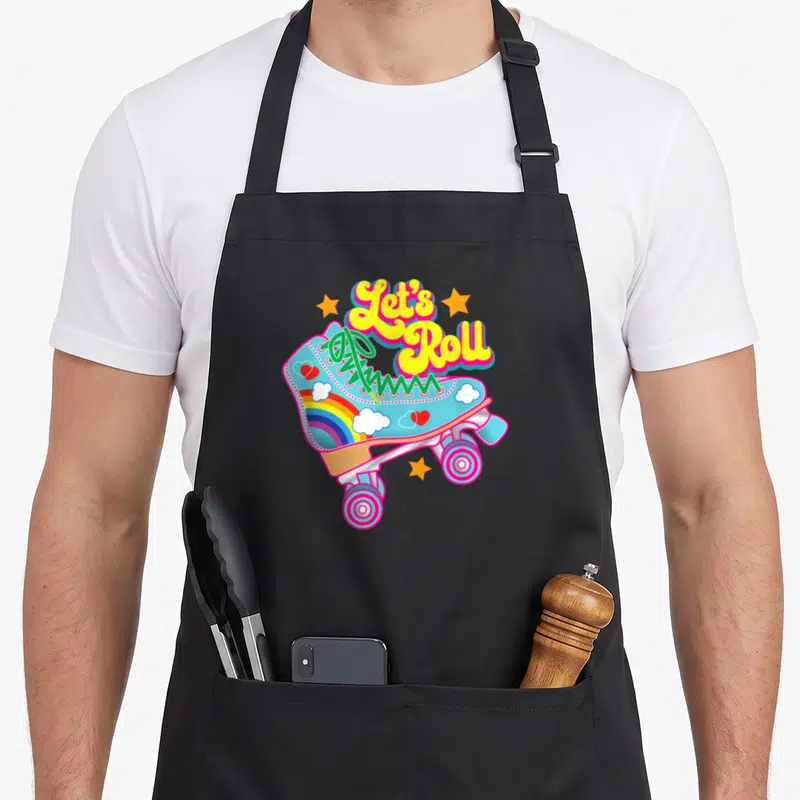 Rollerskating 70s apron - Arched Let's Roll text above light blue skate with rainbow, clouds, hearts, and three orange — shown on a black cotton canvas apron against a white background