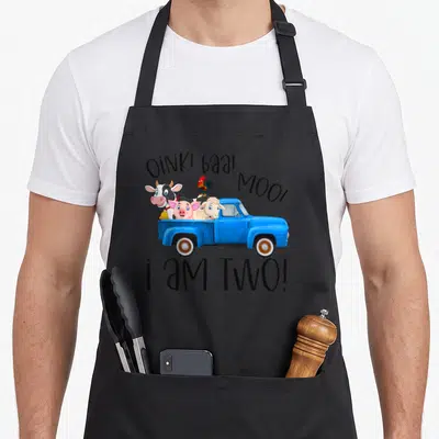 Oink farm aprons - Blue truck with pig cow sheep rooster and text OINK baa MOO i AM TWO — shown on a black cotton canvas apron against a white background