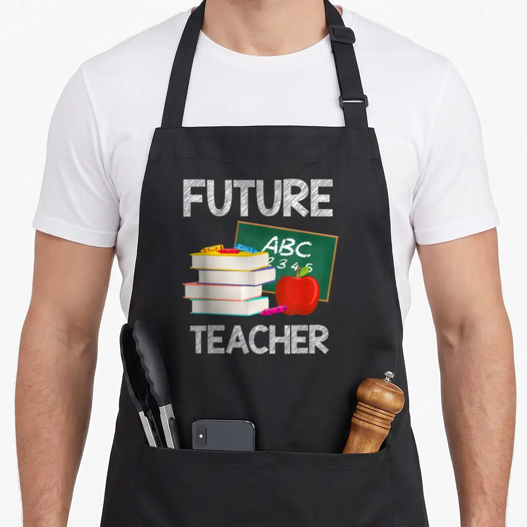 Lesson 1st teacher apron - Stack of books apple and chalkboard with ABC 2345 text — shown on a black cotton canvas apron against a white background