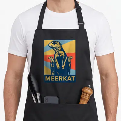 Meerkat animal idea apron - Three meerkats standing against yellow red and blue sunburst with MEERKAT text bar — shown on a black cotton canvas apron against a white background