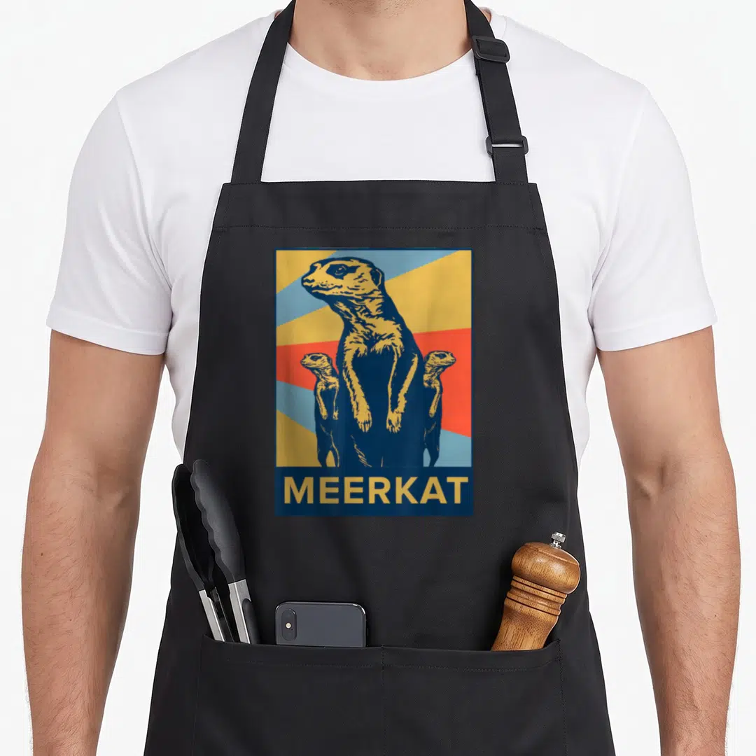 Meerkat animal idea apron - Three meerkats standing against yellow red and blue sunburst with MEERKAT text bar — shown on a black cotton canvas apron against a white background