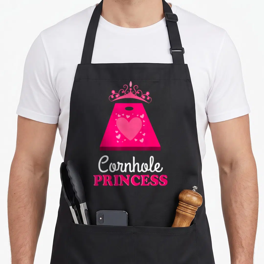 Cornhole princess apron - Pink cornhole board with crown, hearts, and text — shown on a black cotton canvas apron against a white background