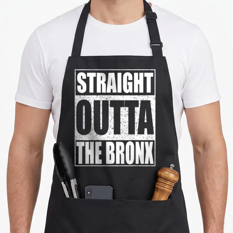 Straight new york apron - STRAGHT OUTTA THE BRONX stacked white and grey typography inside rectangular border — shown on a black cotton canvas apron against a white background