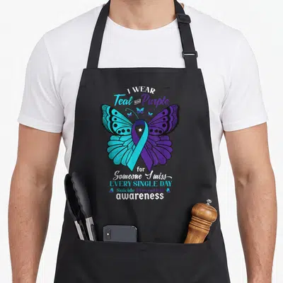 Suicide mental health awareness apron - Teal and purple butterfly with ribbon body and text honoring someone missed — shown on a black cotton canvas apron against a white background