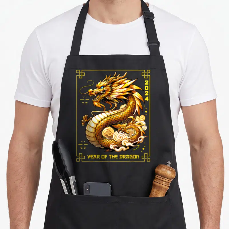 Chinese lunar dragon apron - Coiled gold dragon with white clouds, 2024 text, and YEAR OF THE DRAGON in yellow border — shown on a black cotton canvas apron against a white background
