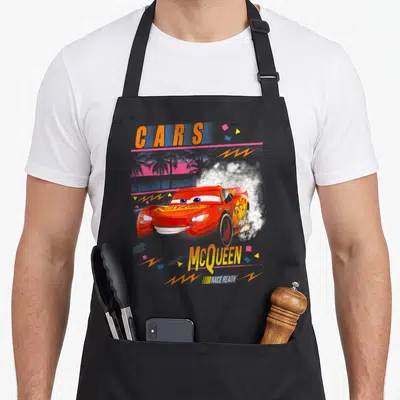 Palm car apron - Red race car with CARS McQUEEN RACE READY text over pink palm tree and white smoke with geometric — shown on a black cotton canvas apron against a white background