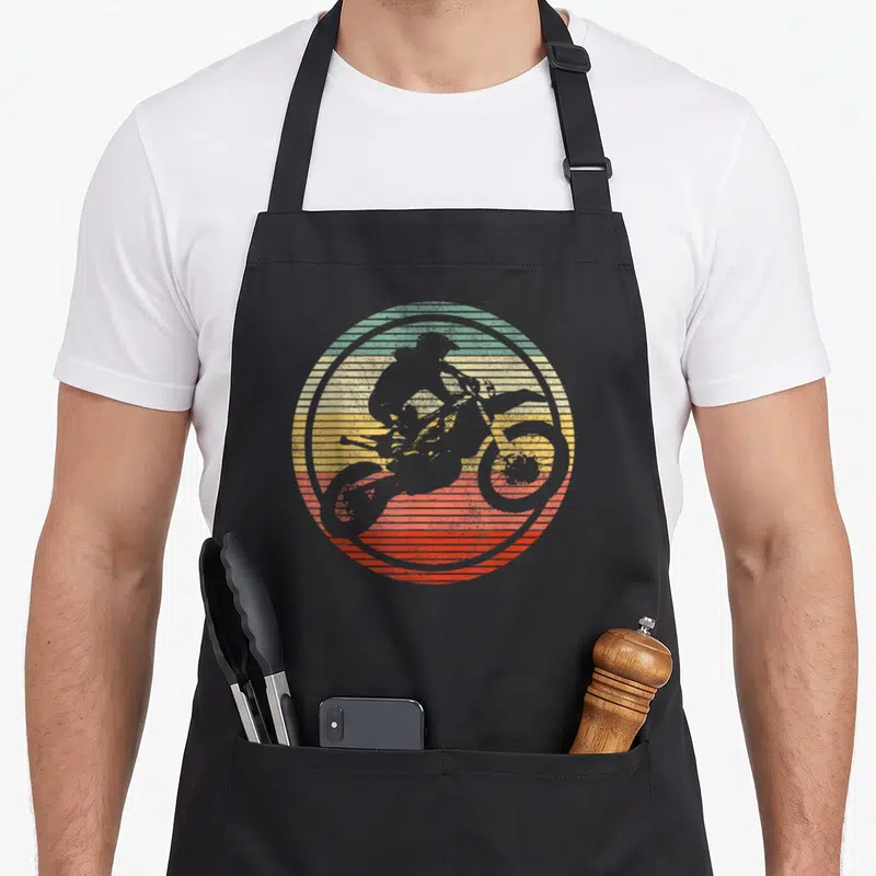 Biker bike apron - Grey motocross rider silhouette over teal yellow orange and red horizontal stripes — shown on a black cotton canvas apron against a white background