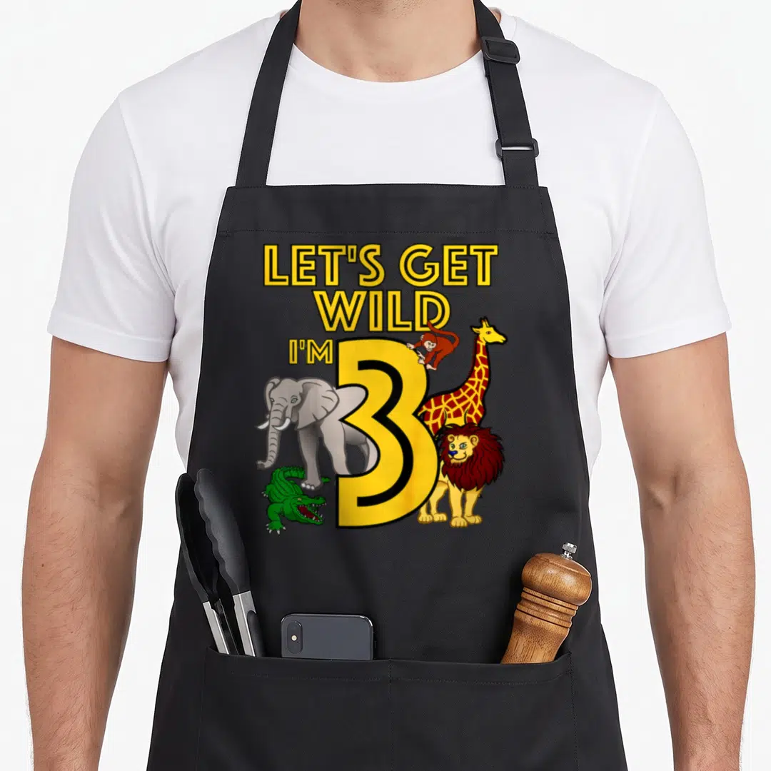 Zoo safari birthday apron - LET'S GET WILD I'M 3 text with elephant giraffe lion crocodile and monkey in cartoon style — shown on a black cotton canvas apron against a white background