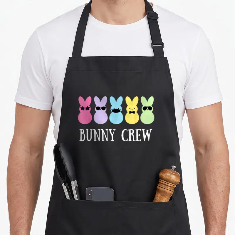 Crew easter bunny aprons - Five colorful cartoon bunny heads wearing glasses, mask, and bow tie above white text — shown on a black cotton canvas apron against a white background