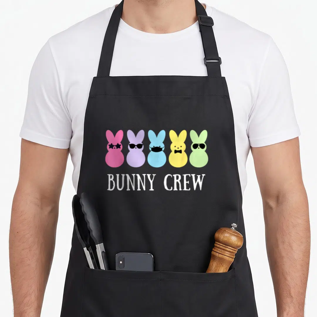 Crew easter bunny aprons - Five colorful cartoon bunny heads wearing glasses, mask, and bow tie above white text — shown on a black cotton canvas apron against a white background