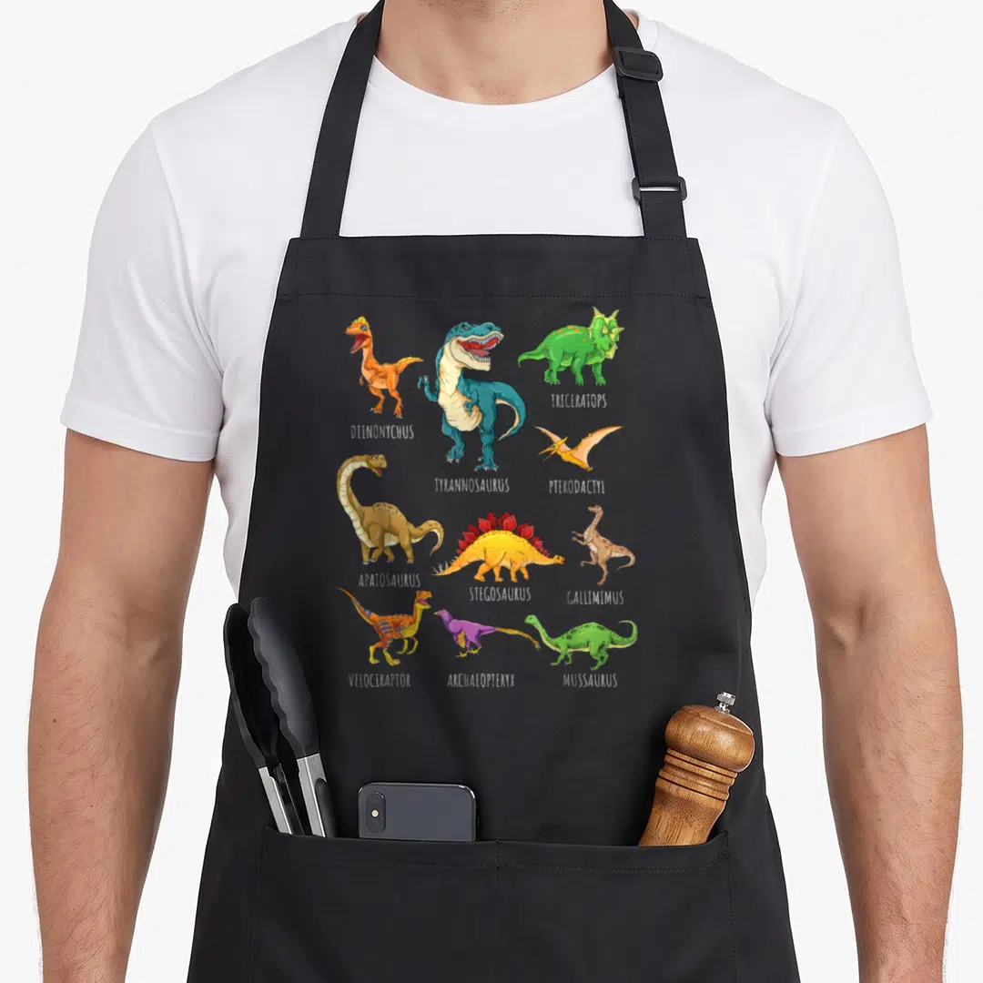 Dino identification dinosaur apron - Ten colorful cartoon dinosaurs with white scientific name labels arranged in three — shown on a black cotton canvas apron against a white background