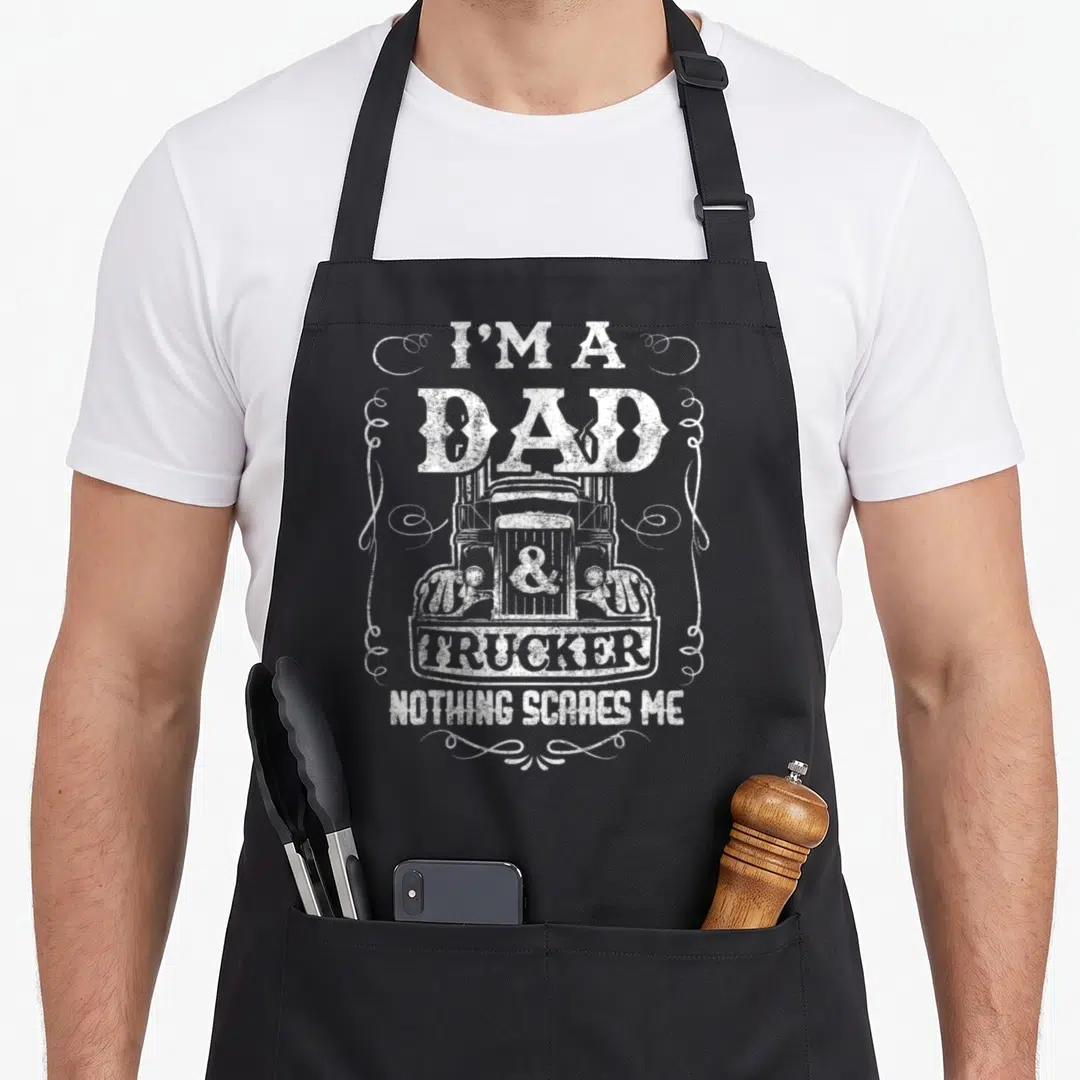 Trucker father day apron - White distressed text I'M A DAD & TRUCKER NOTHING SCARES ME around a truck front with swirls — shown on a black cotton canvas apron against a white background